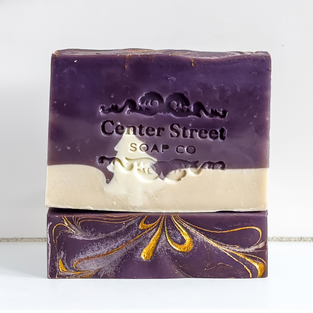 Two rectangular bars of handmade soap stacked vertically. The top bar is solid deep purple with the brand name 'Center Street Soap Co' embossed on the front.