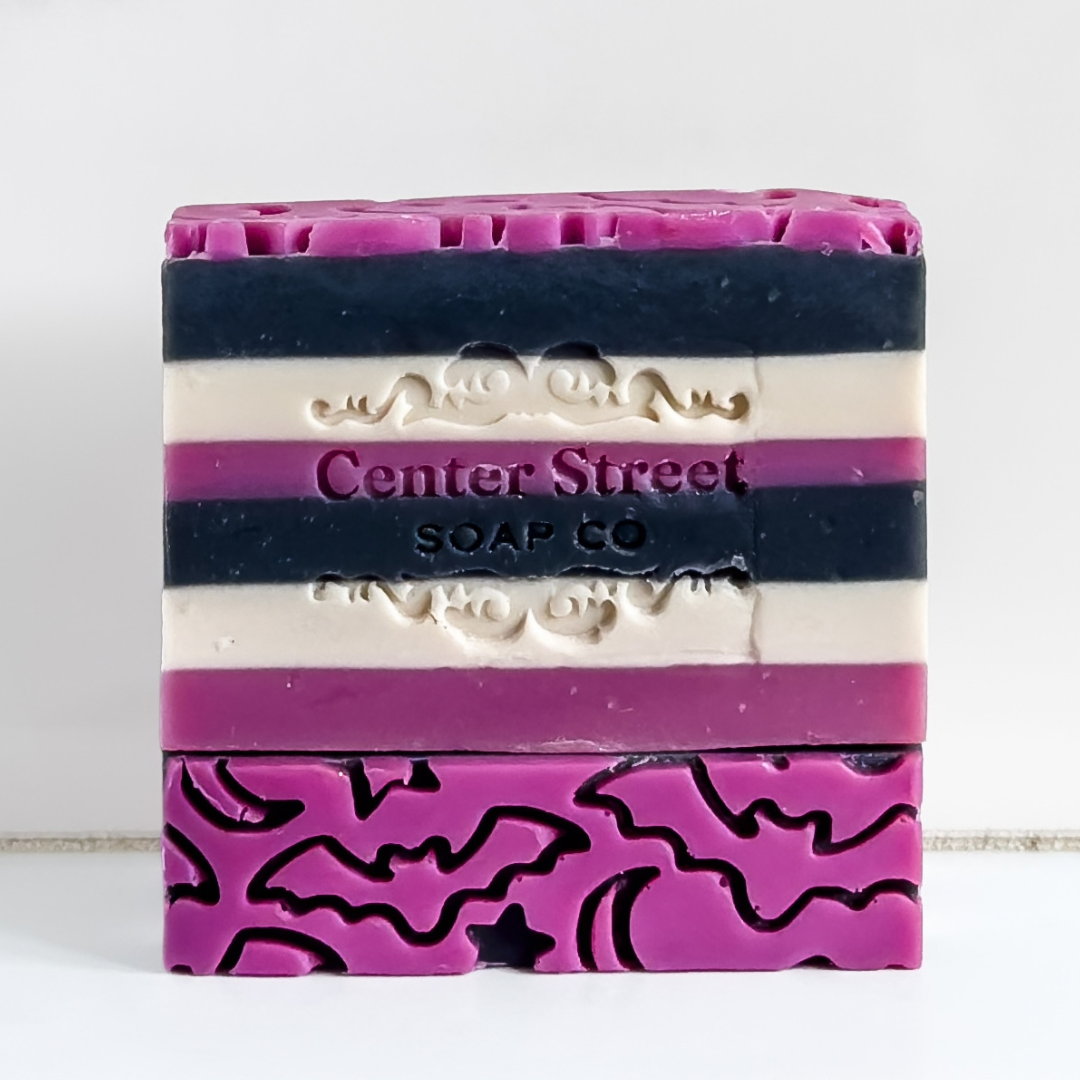A rectangular bar of handmade soap with horizontal stripes in magenta, cream, and dark navy, featuring an embossed logo that reads 'Center Street SOAP CO'. The bottom portion has a magenta section with black wavy line patterns.